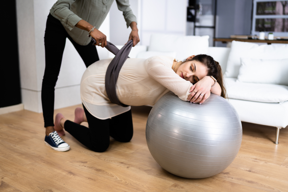 A pregnant woman kneeling and resting upon an exercise ball